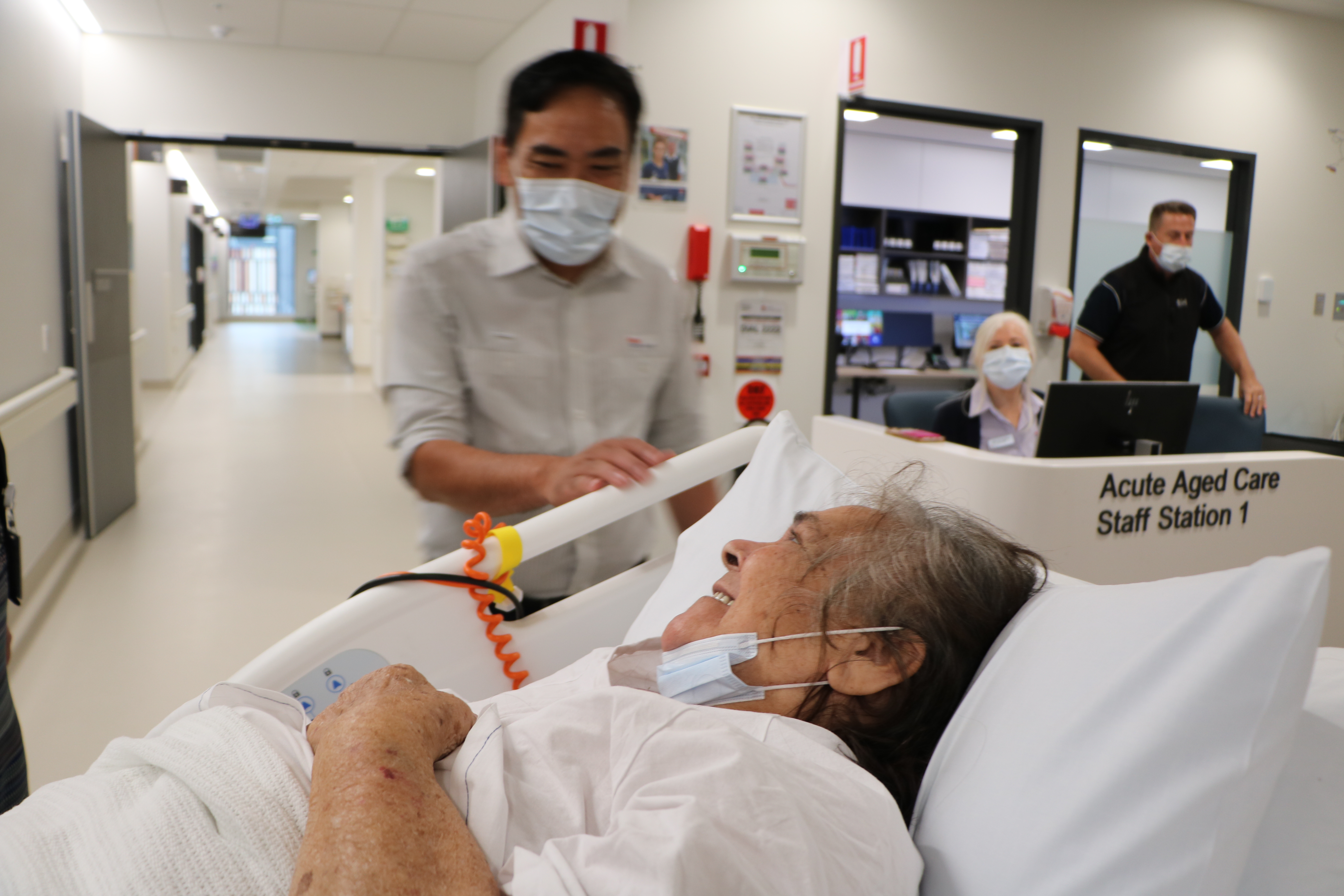 Lady in hospital bed with smiling staff, moving into new building